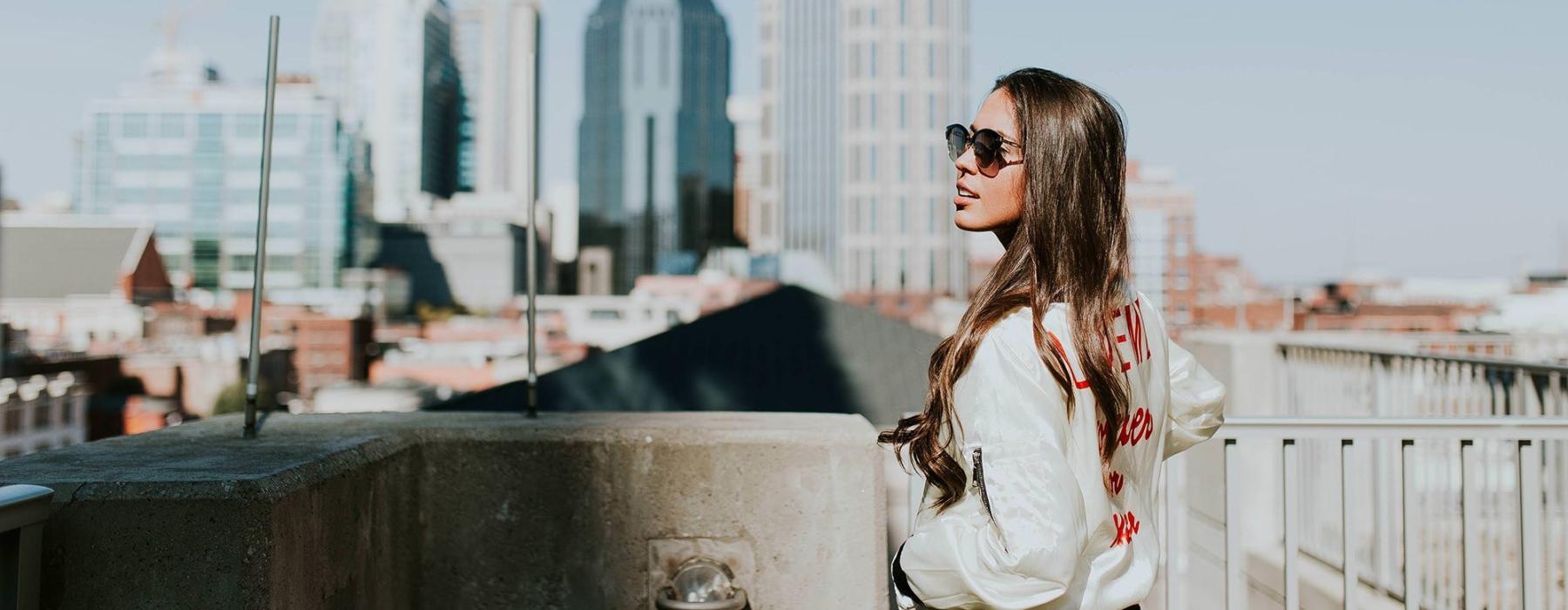 woman with sunglasses stands on a rooftop overlooking the city